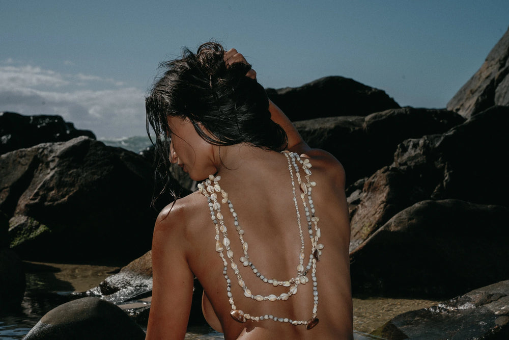 a woman's back in front of the ocean with strands of pearls
